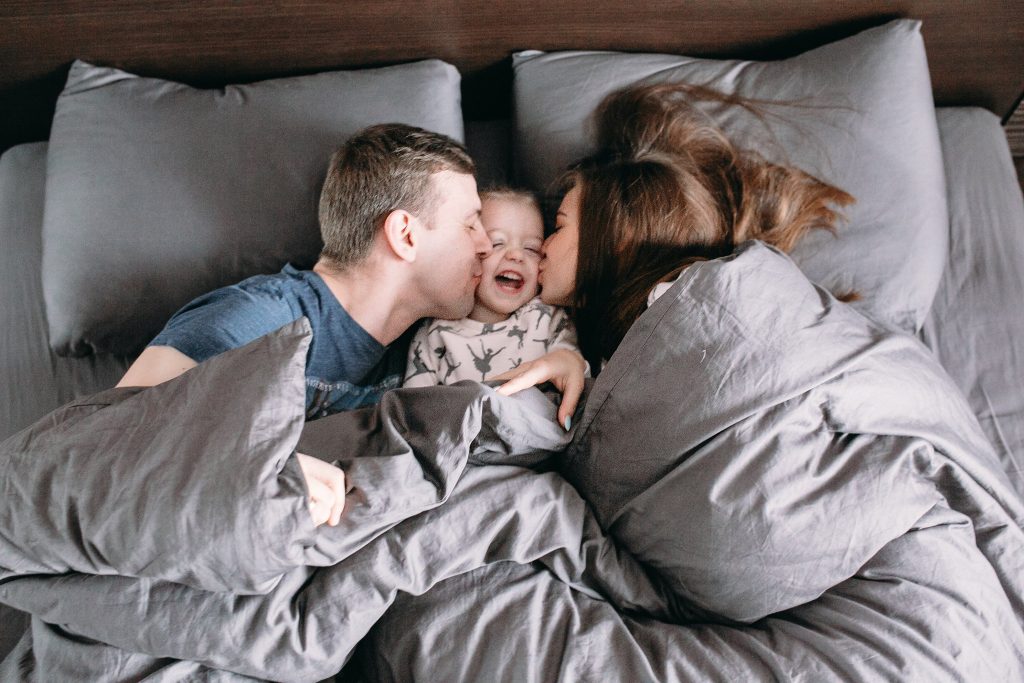 Family in bed, couple kissing their daughter in bed